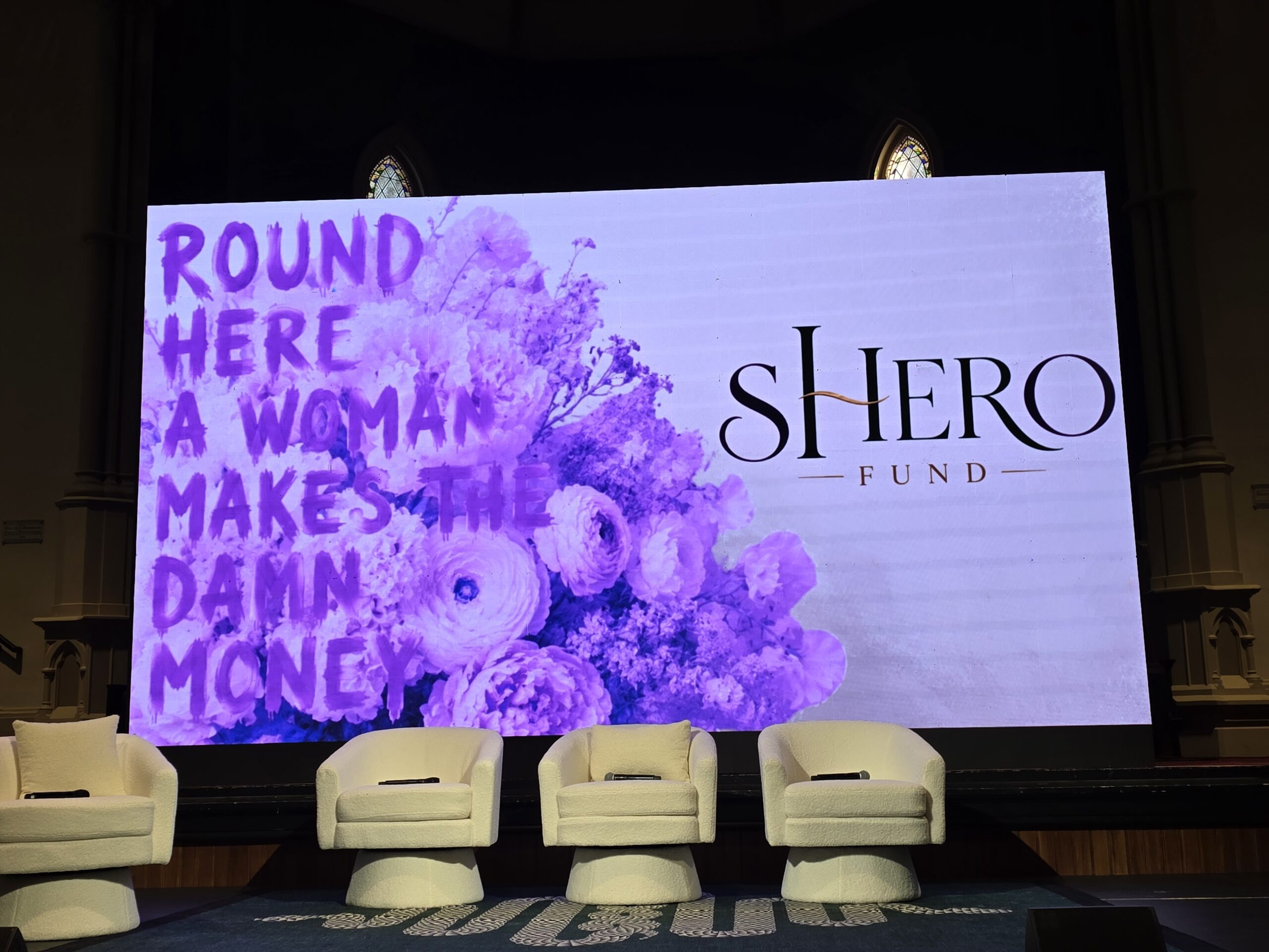An empty stage with a screen that says "Round here women make the damn money"
